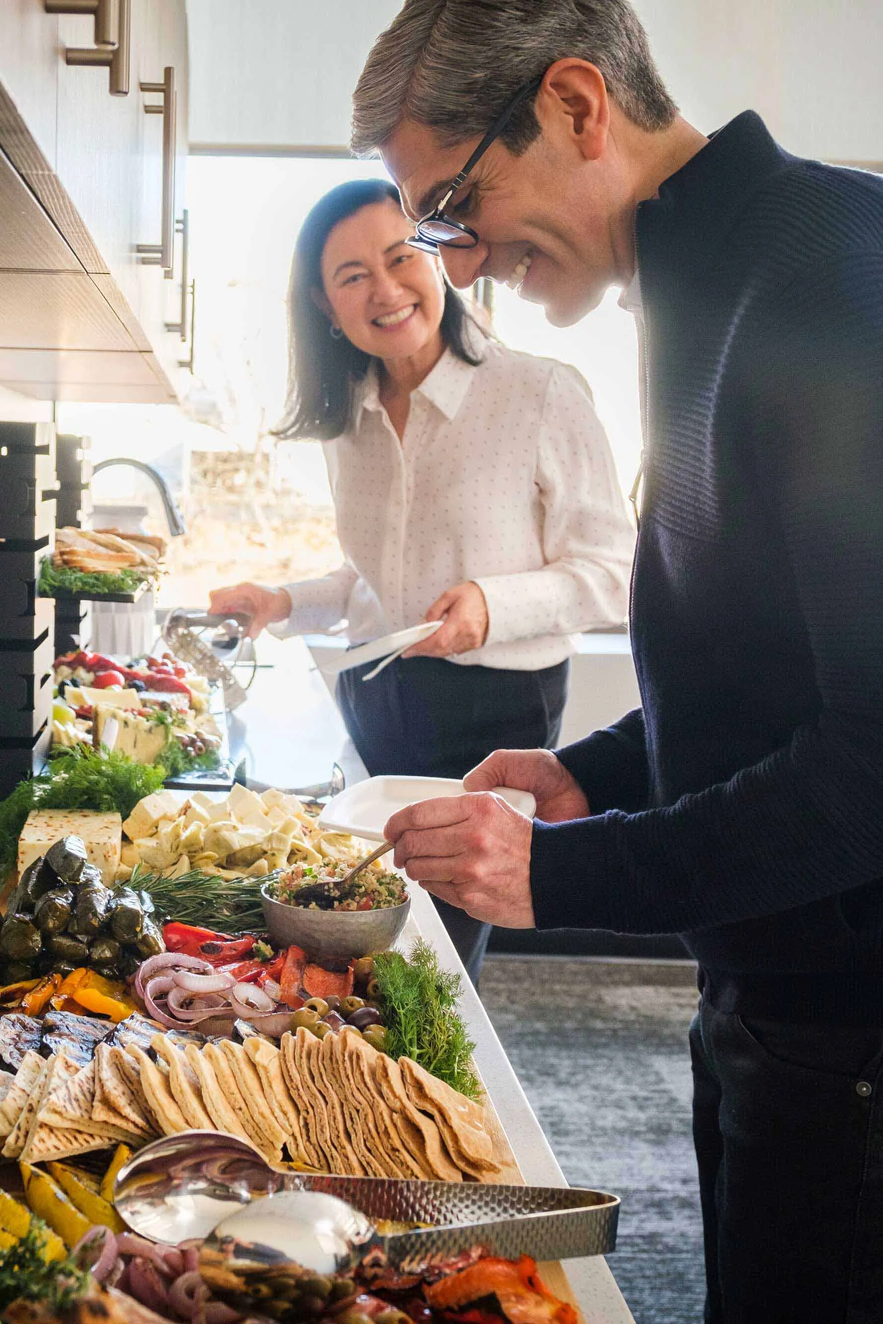 Two office workers smiling while grabbing food from a catered buffet